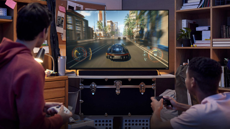 Two young people play a videogame on a television in a small room.