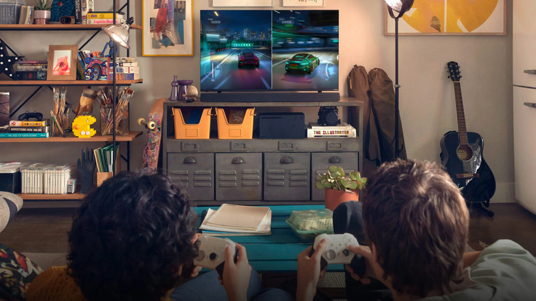 Two young people play video games on a small TV in a busy room