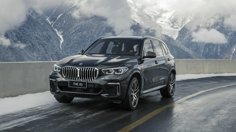 A 2021 BMW X5 driven on a snowy mountain road with white clouds and hills in the background.