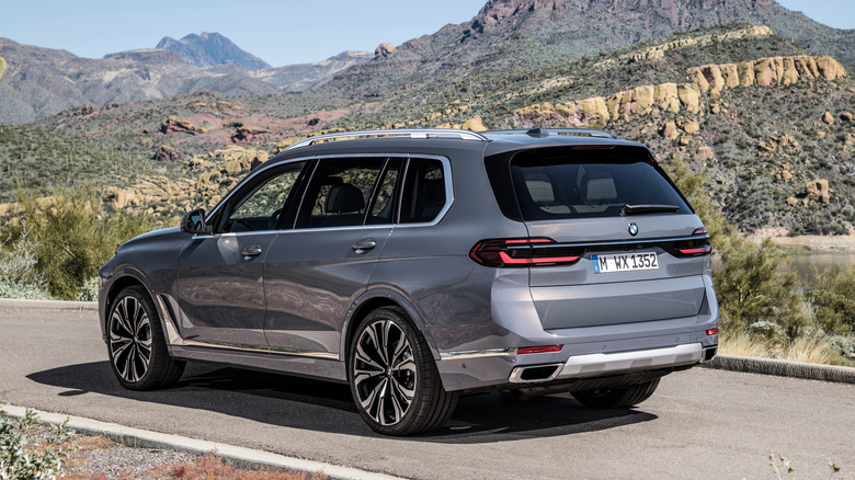 A rear three-quarter view of a gray BMW X7 parked on a rural road with hills in the background.