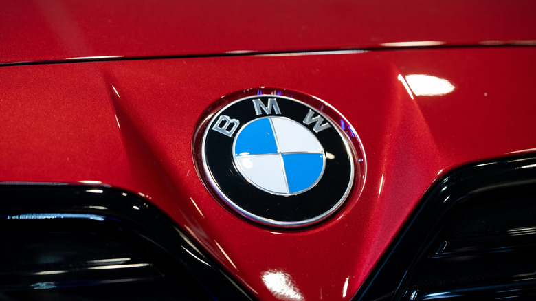 A close-up of a BMW badge on a red BMW front bumper and hood area.