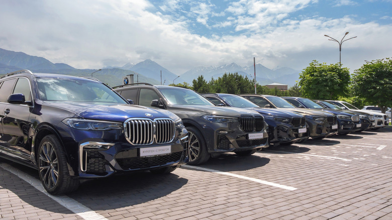 A row of various BMW SUVs parked next to each other in an outdoor cobblestone parking lot.