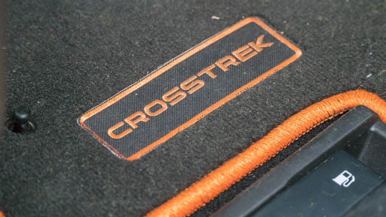 A black Subaru Crosstrek floor mat with an orange Crosstrek marking.