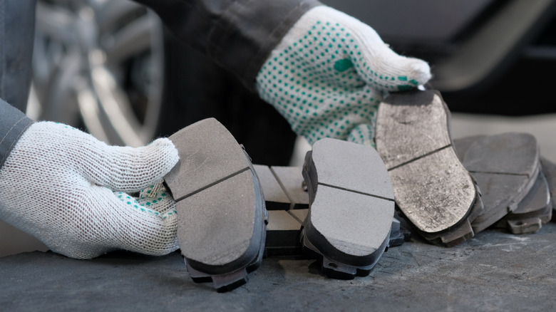 A person wearing gloves showcasing different types of car brake pads.