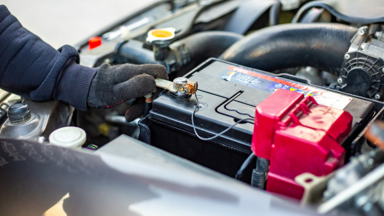 A mechanic wearing gloves loosening car battery terminal screws.