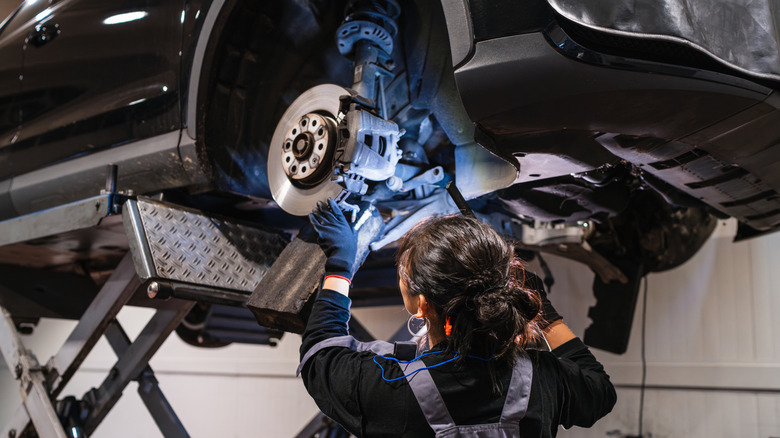 A female mechanic looking underneath a car on a car ramp in a workshop.