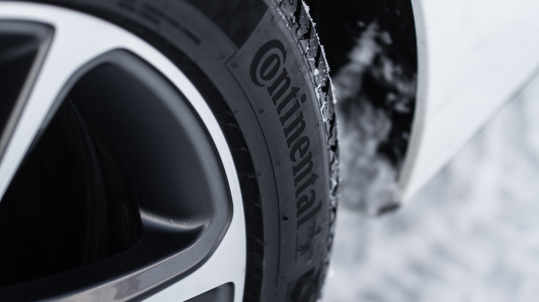 A close-up of a Continental winter tire mounted on a white vehicle with snow on the ground.