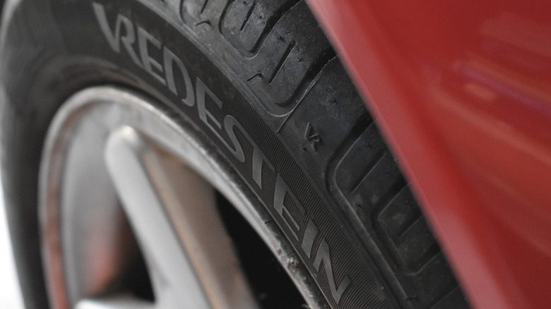 A close-up of a Vredestein tire mounted on a wheel of a red car.