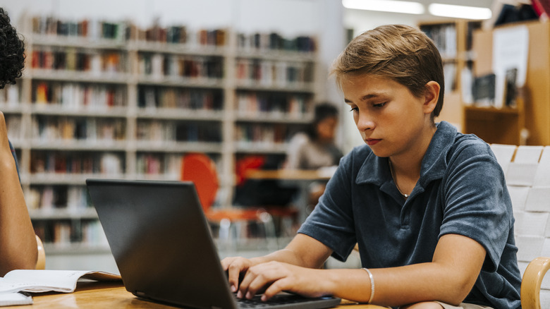 middle school student using laptop in library