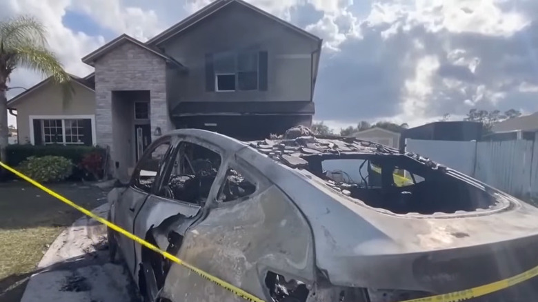 Burnt-out Tesla in front of a fire-damaged house