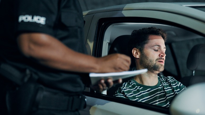 A police officer writinc a ticket for a traffic offender sitting inside a car