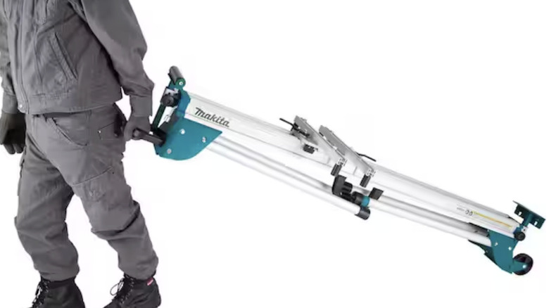 A man toting a folded Makita folding miter saw stand behind him