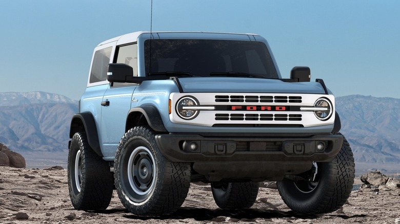 A bright blue two-door Ford Bronco parked in the wild with mountains in the background