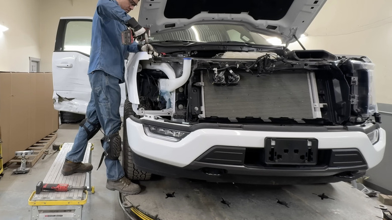A technician repairs a white Ford F-150 at a repair shop