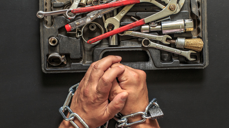A man's hands are chained as he tries to access his toolbox