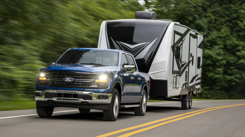 A blue 2024 Ford F-150 towing a large camper, front 3/4 view