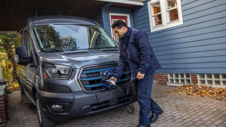 A person charging the Ford E-Transit truck in front of a house.