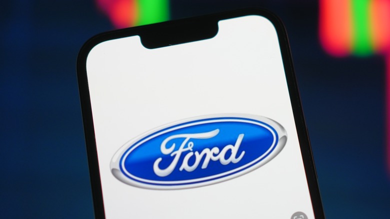 A cell phone displaying the Ford logo with red and green lights in the background