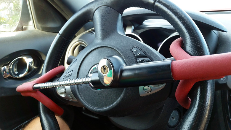A close-up of a black steering wheel inside a vehicle with a red and black steering wheel lock attached