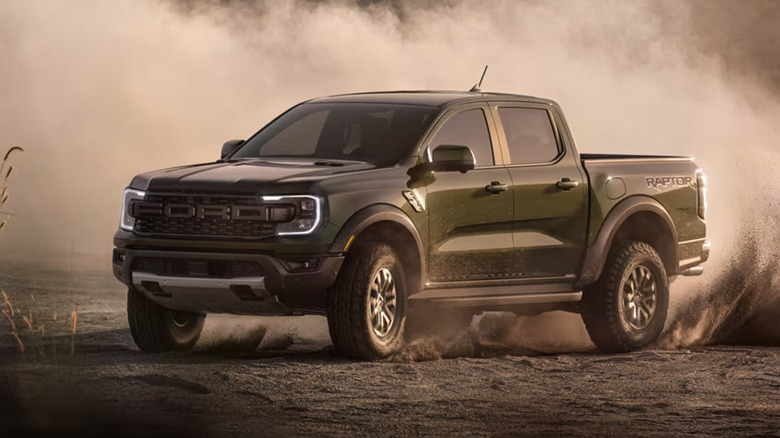 Dark green 2026 Ford Ranger Raptor off roading, blowing dirt high into the air, front 3/4 view