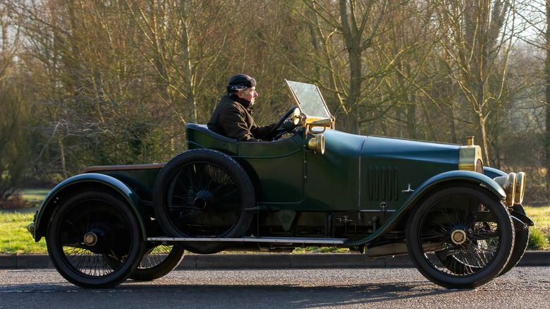 Side shot of man in leather cap driving green Ford Model T