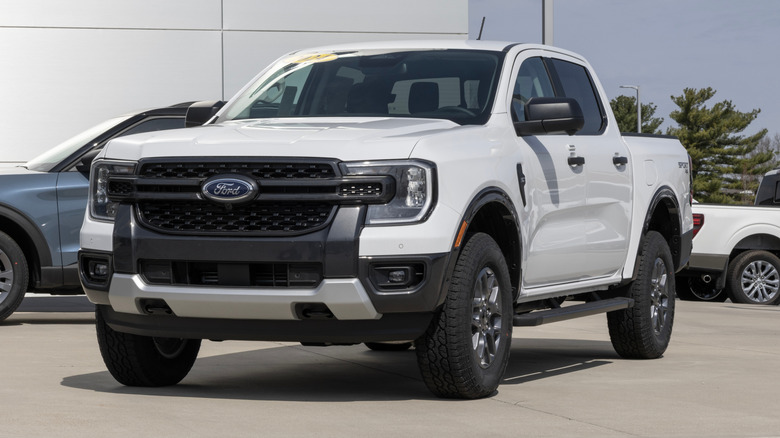 Front 3/4 view of white Ford Ranger pickup parked in front of Ford dealership.
