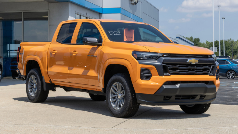 Front 3/4 view or orange Chevy Colorado pickup truck parked at a Chevy dealership.