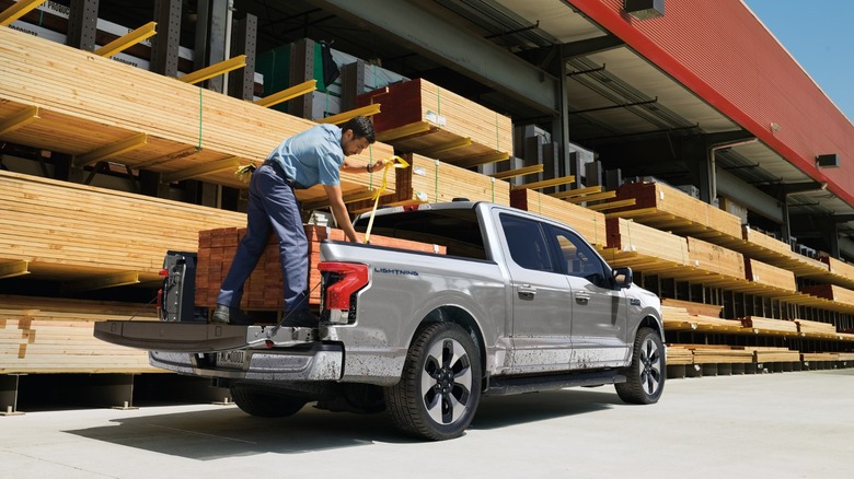 Man loading lumber into the bed of a silver Ford F-150 Lightning at a lumberyard
