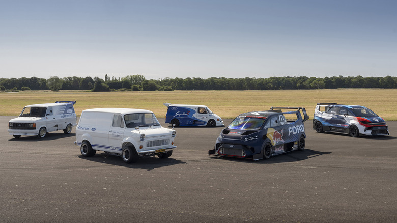 One of each version of Ford Supervan parked in asphalt lot near open field
