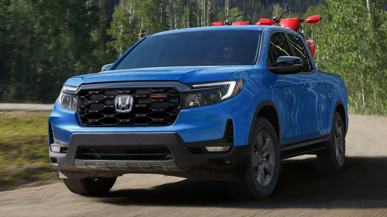 3/4 shot of a  Diffused Sky Blue Pearl 2024 Honda Ridgeline TrailSport on a road with trees and mountains in the background