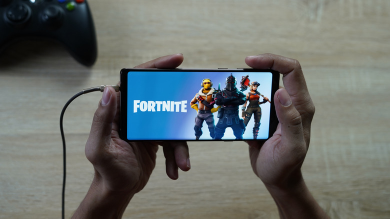 Boy playing Fortnite on his phone with a game controller seen in the background.