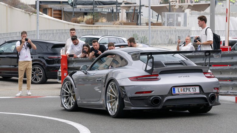 A silver Porsche 911 GT2 RS being driven through Monaco with car spotters taking pictures.