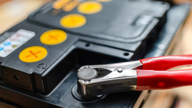 A close-up of a black and yellow car battery with a red clamp attached to its positive terminal.