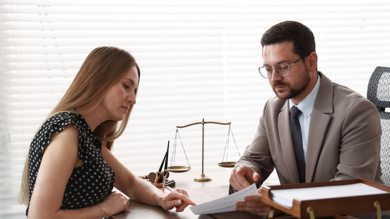 A lawyer in a suit reviewing documents with a client at an office desk with scales of justice