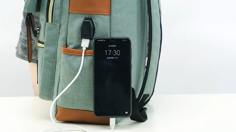 USB cable comes out of a backpack, charging a phone nearby