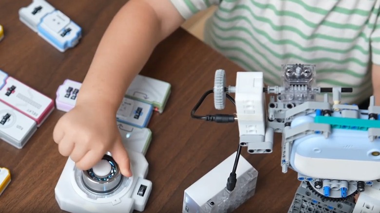 Child's hands twisting a dial on a table containing multiple white tile-shaped pieces