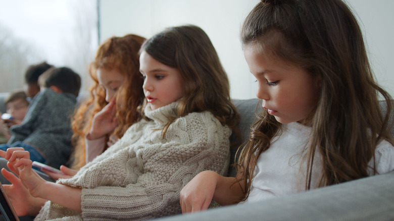 Young children sitting on a sofa playing with screen-based electronic devices