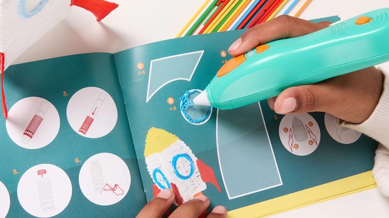 Child's hands using a green pen-like tool to 3D print on a book