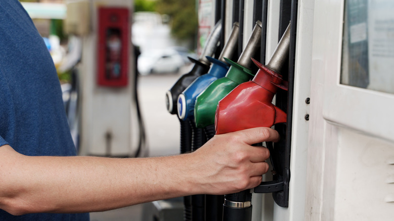 A person reaching for a gas pump nozzle.