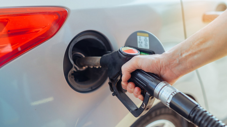Close up of a hand holding a gas nozzle and refilling a white car
