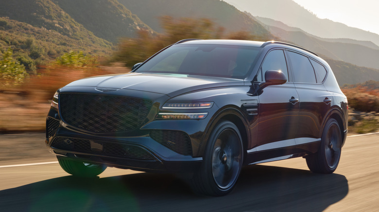 Front 3/4 view of 2026 Genesis GV80 driving on road in mountainous area