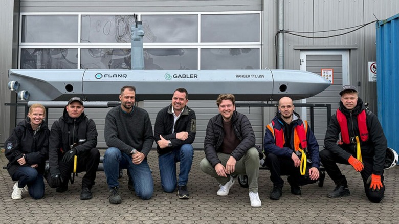 A Torpedo-Tube-Launched Uncrewed Surface Vessel (TTL USV) drone with the team that designed it smiling together
