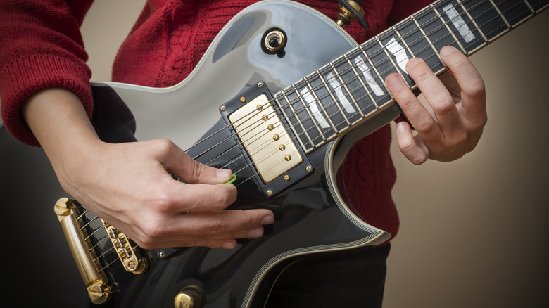 A close up shot of a woman playing a slate grey les paul with a green pick.