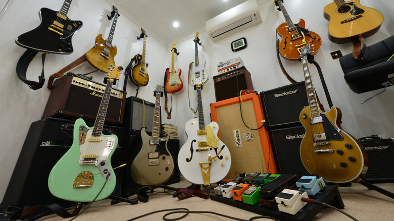 A variety of guitars, including a handful of gibons (hollow bodies and les pauls), alongside a wall of amps and a full pedal board.
