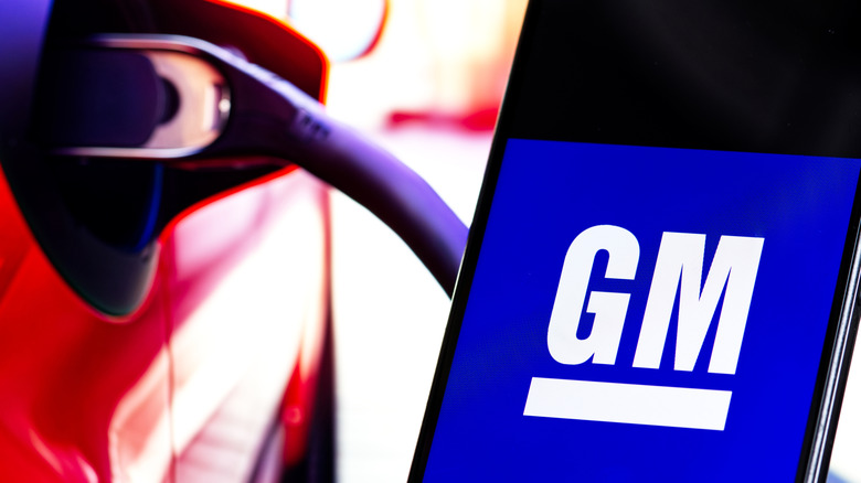 GM logo on a smartphone screen next to a charging plug on an EV