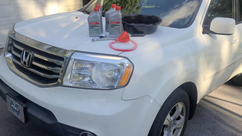 A white Honda SUV with transmission fluid, an oil pan, wrenches, and a funnel laid out on its hood.