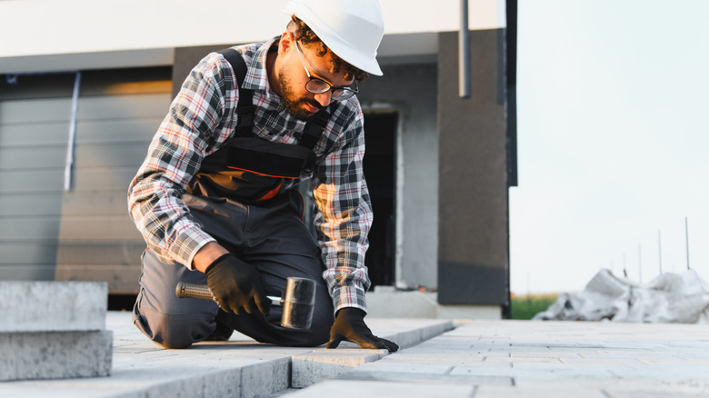man in a white construction hat trying to install permeable pavers