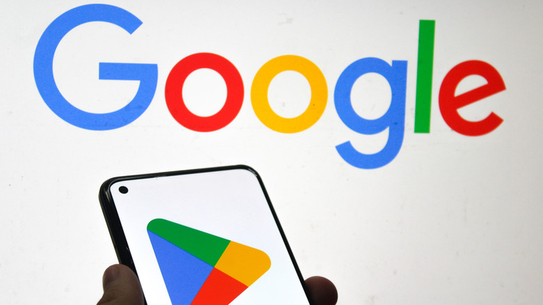 Google Play Store logo on a mobile phone screen with Google company logo in the background