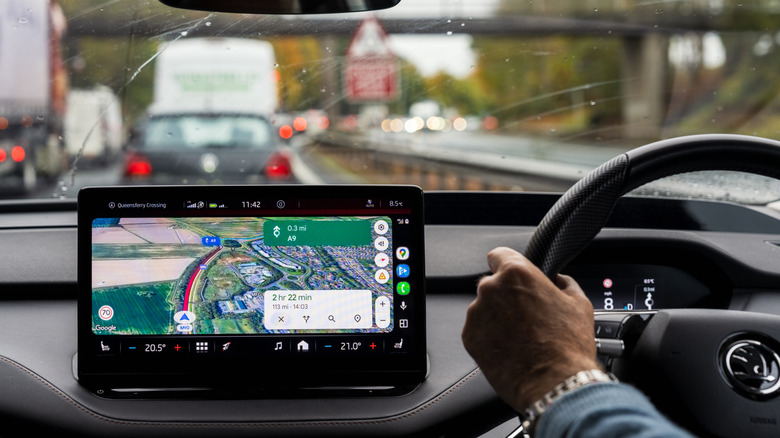 Person driving in heavy traffic with Google Maps on display on central infotainment system