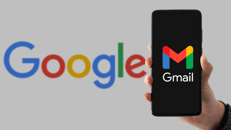 Hand holding up a smartphone showing Gmail logo with Google logo in background